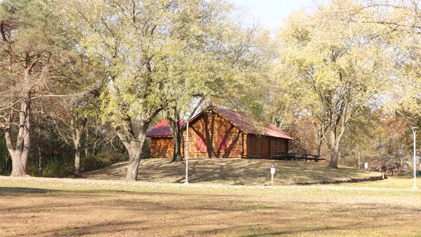 Beautiful autumn day view of a log shelter building in park. Sun creating shadows across grass.