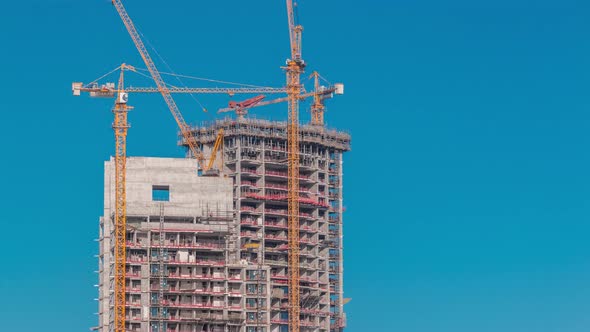 Aerial View of a Skyscraper Under Construction with Huge Cranes Timelapse in Dubai Marina alt