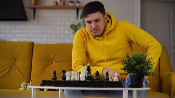 Young Man Sitting on Yellow Sofa and Playing Chess in Room alt
