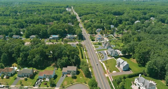 Flight with a Drone Over a with Low Houses in Monroe Town on a Sunny Day on Between the Forest alt