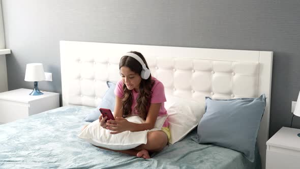 Happy Teen Girl Has Video Call Listening Music in Headphones in Bedroom Technology