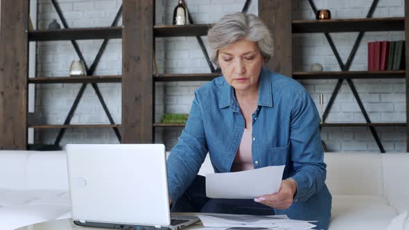 Sad Elderly Retired Woman with a Depressed Look, Calculating the Family Budget, Sitting on the Sofa alt