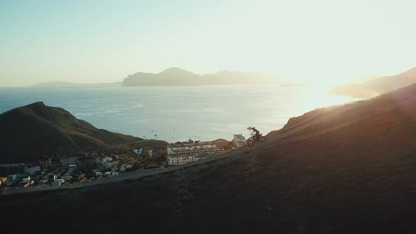 Drone View of Man on Motorbike Extremely Rides Across the Hills with Black Sea on Background in