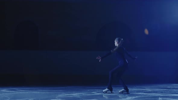 Professional Figure Skating Artist Slides and Spins on Ice Arena in Rays of Blue Light alt