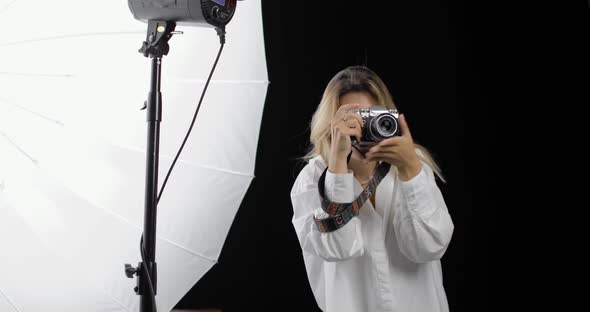 Young Woman Photographer in a White Shirt with Long Blond Hair Works with Enthusiasm Making Shots