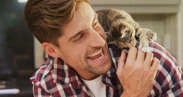 Smiling young man playing with his pet cat in the kitchen 4K 4k alt