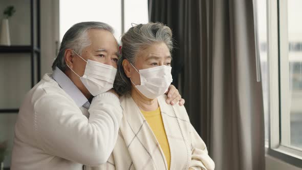 Two elderly Asian couples wearing masks hug and encourage each other.