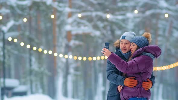 Lovely Couple Makes Selfie with Phone Kissing in Snowy Park