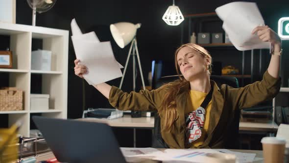 Portrait of Happy Young Woman Throwing Papers in Night Office in Slow Motion alt