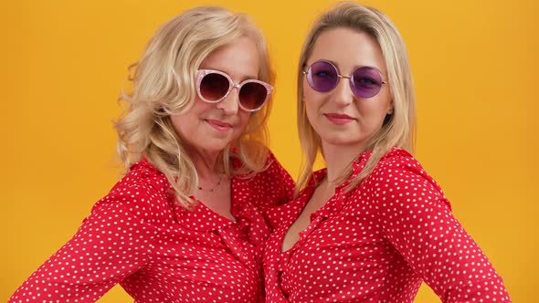 Two Blonde Beautiful European Women in Their 40s Standing Close to Each Other Wearing Similar Red alt