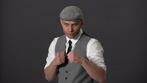 Portrait of Concentrated English Hooligan in Formal Suit and Flat Cap Clenching Fists and Ready for alt