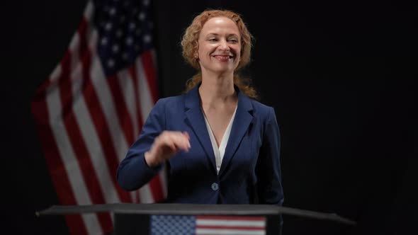 Happy Politician Woman Showing Support Gesture Looking Around Standing in Camera Flashes at Black alt