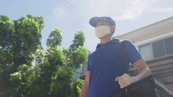 Asian delivery man in blue uniform with face mask carrying bag of food delivering food to customer. alt