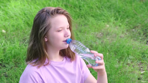 Girl Drinks Clean Drinking Water From a Bottle in a Green City Park on a Hot Summer Day