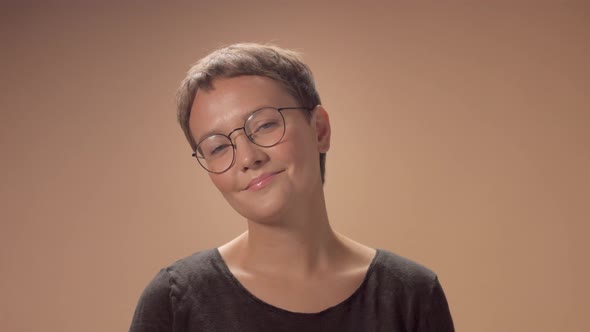 Caucasian Woman with Short Haircut Wears Glasses in Studio on Beige Background
