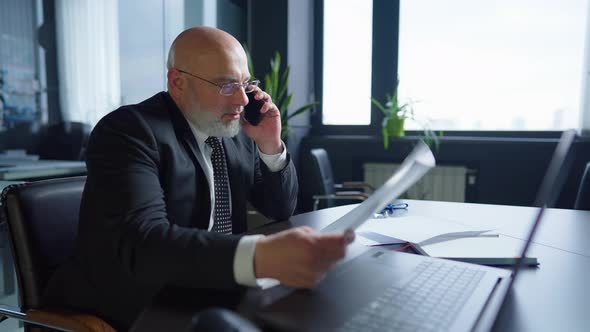 Confident Intelligent Professional Businessman Talking on the Phone Analyzing Graph Sitting at Table alt