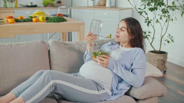 Pregnant Woman With Great Pleasure Eating Vegetable Salad on the Couch alt