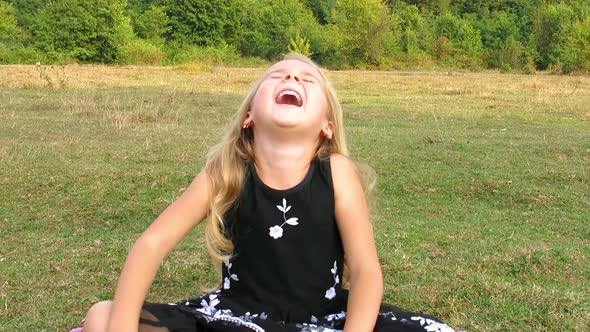 Girl Sitting on the Grass and Bursts out Laughing. Irrepressible Girl's Laugh. alt
