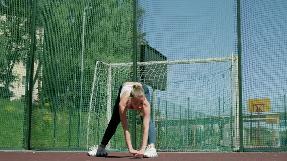 Young Sporty Blond Girl in Sportswear Does Exercises Outdoors at Sports Ground