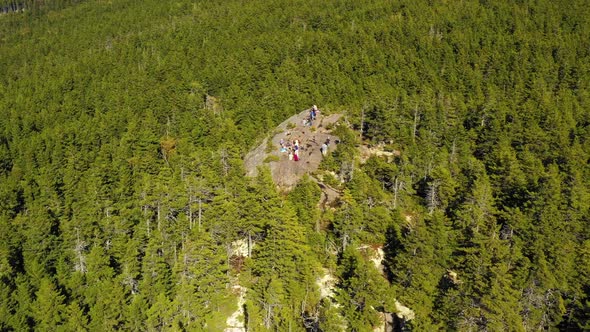 Aerial drone shot over the green and autumn colored forest and a group of hikers on a rocky outcrop alt
