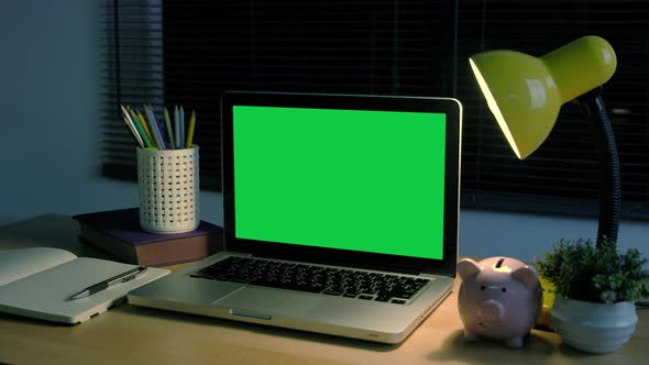 Chroma key green screen laptop computer set up for work on home office at night.