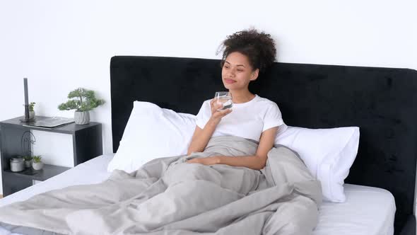 Beautiful Satisfied African American Girl in a White Tshirt Sitting in a Bed in the Morning Holds a alt