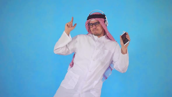 Arab Man in Headphones Stands on a Blue Background and Vigorously Dancing To the Music alt