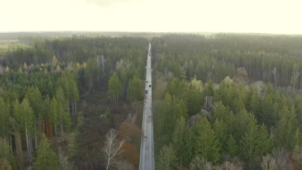 Pullback shot of a drone over a autumn colored forest tracking a transporter car while flying backwa alt