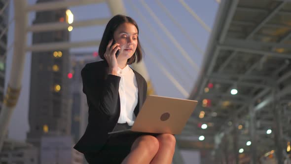 Caucasian beautiful business woman working and typing on computer sitting outdoor at night in city. alt