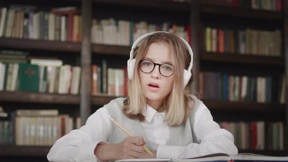 Schoolgirl Pupil Wearing Headphones Writes Notes in a Notebook Distance Learning Online at Virtual alt