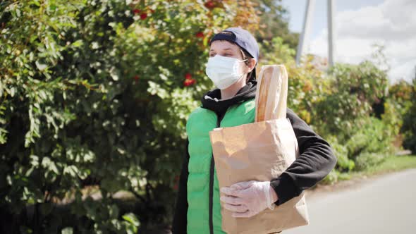 Courier in Protective Medical Mask and Gloves Holding Bag with Foods alt