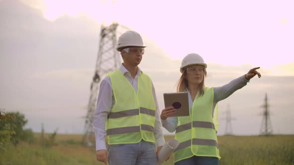 Engineers in Uniform Working with a Laptop Near Transmission Lines alt