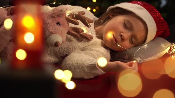 Girl Sleeps on Background of Christmas Tree and Waits for Santa Claus and New Years Gifts alt