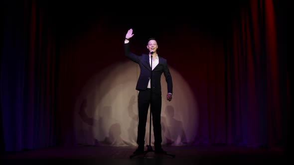 Man in Suit Stand Up Comedian Speaking Jokes in Micropphone Standing on Stage. alt