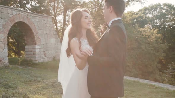 Groom Comes To Bride, Who Poses in White Dress and Kisses Her alt