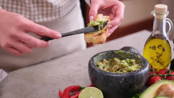 Woman Making Bruschetta with Freshly Made Guacamole Sauce at Domestic Kitchen alt