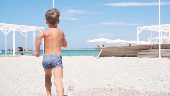 Happy Little Boy Runs Along the Seashore on the Beach. alt