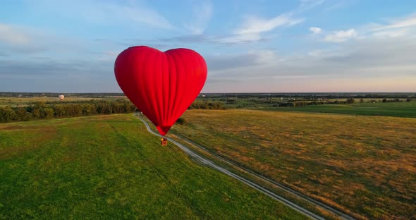 Hot air balloon flying over field. Romantic red aerostat in the heart shape moving slowly in the air alt