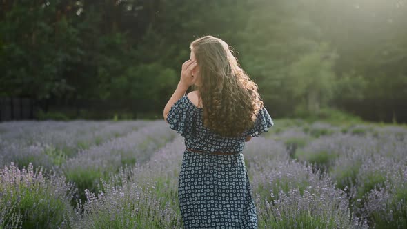 Curly Brunette Young Girl Walks in a Lavender Field Smiles Looks at the Camera Back View Sunny