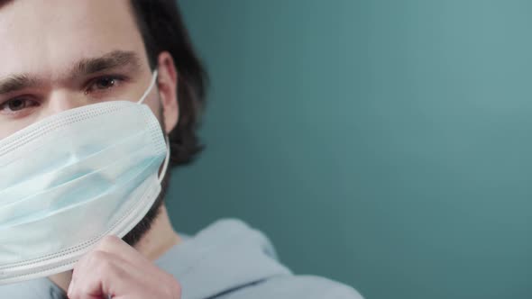 Charming Dark Haired Man Dressed Light Hoodie Putting on a Protective Face Mask
