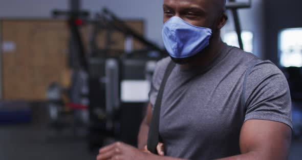 Fit african american man wearing face mask sneezing on his elbow in the gym alt