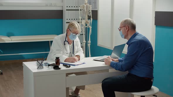 Health Specialist Taking Notes at Consultation Appointment with Old Man alt