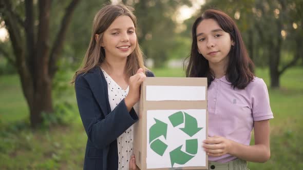 Two Confident Caucasian Teenage Girls Posing with Box with Green Recycling Sign in Spring Summer alt