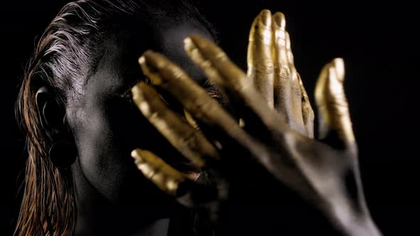 Portrait of a Young Woman with Black Paint on Her Face and Golden Hands and Lips alt