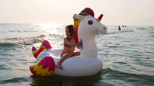 Three year old girl happily plays with her inflatable unicorn.