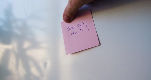 You Can Do It  a Man's Hand is Pasting a Reminder Sticker alt