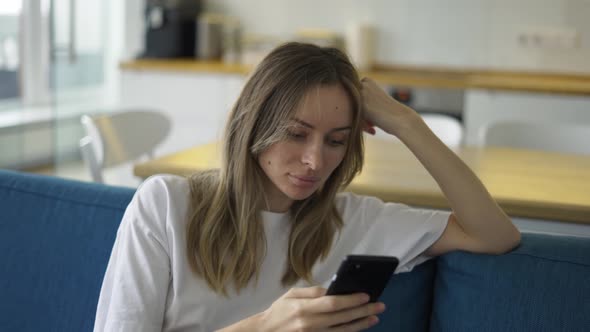 Calm Woman Surfing in Internet at Phone in Apartment on Couch alt
