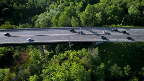Convoy of vehicles in pursuit over highway bridge through lush green forested landscape, fast tracki alt