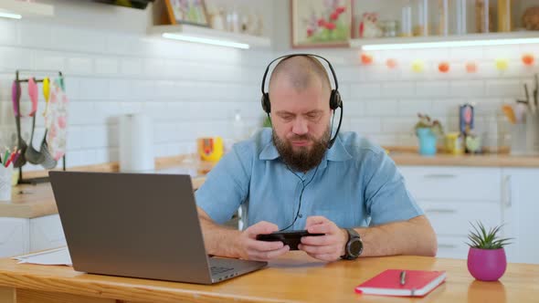 Cheerful Mature Man Emotionally Playing a Game on His Phone During Work Break While Sitting alt