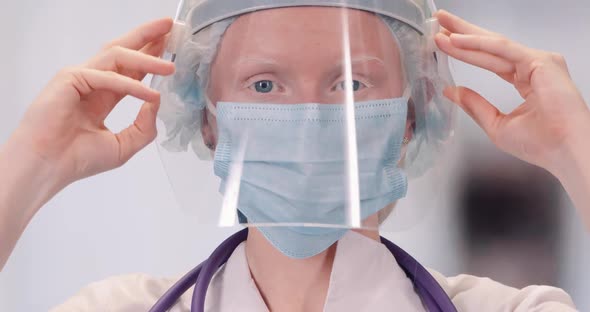 Portrait of Young Female Doctor in Protective Gear and Medical Mask, Albino Woman Puts on a Plastic alt
